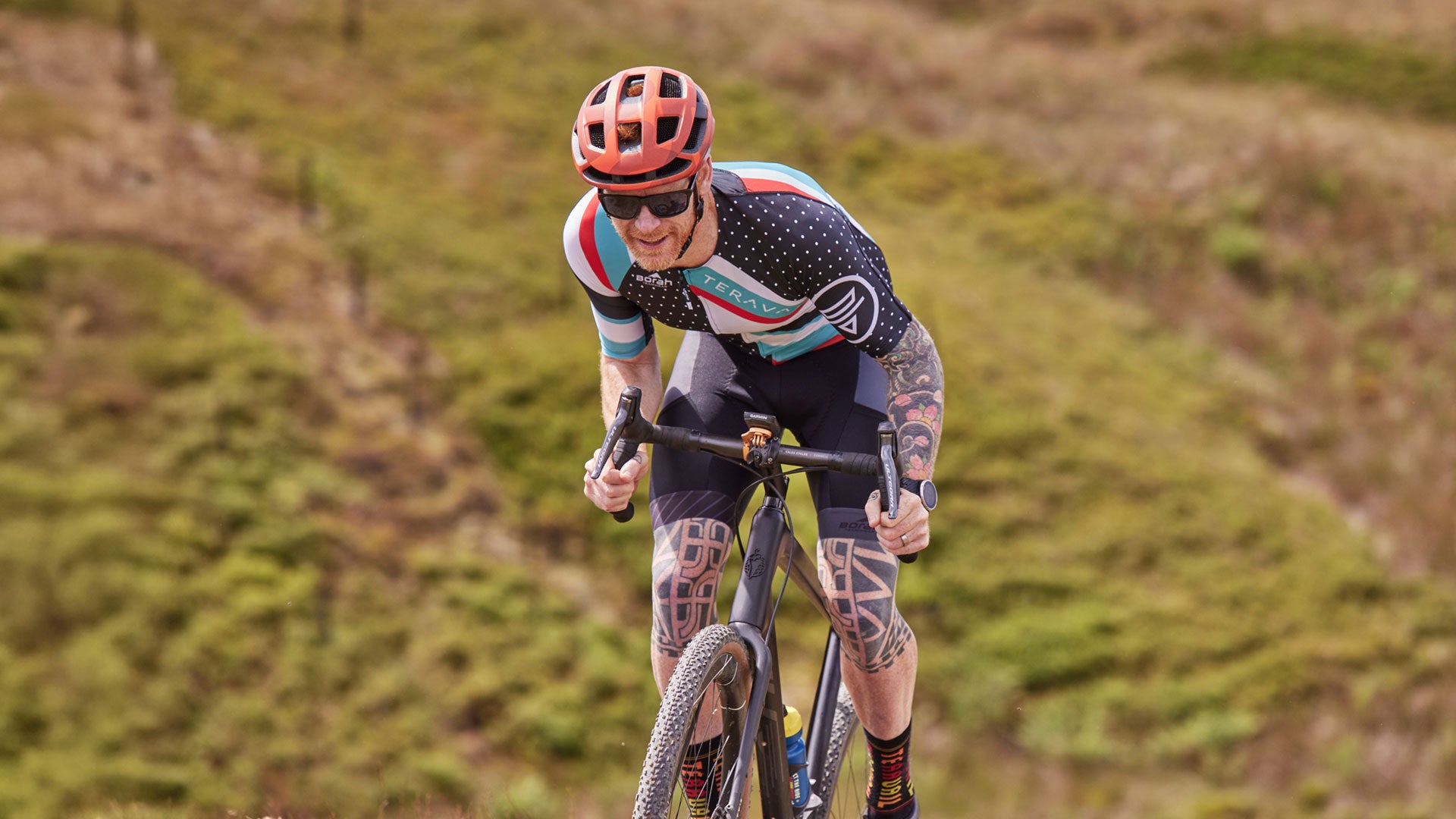 Cyclist out of saddle climbing gravel road wearing Teravail jersey and bib shorts